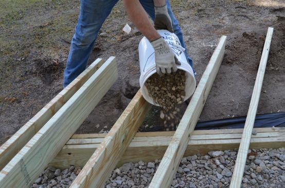 Finlay's crew placed crushed stone around the beam for free drainage and frost protection, not for load-bearing purposes: the steel brackets of the helical piers, driven to below the frost line, are the deck's structural support.