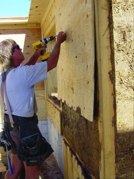 A trainee removes temporary formwork from the outside of the Larsen-truss double wall after clay and straw have set up and dried.
