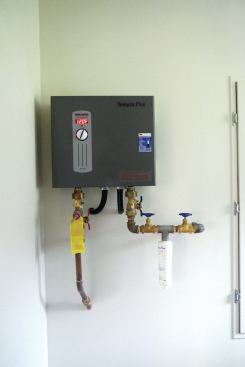 The Stiebel Eltron Tempra 24 Plus on-demand water heater has a water-temperature dial and LED ridge. As part of the installation, the author included an Aqua-Pure AP430SS Scale Inhibition System, which has a consumable water-treatment (white) canister.