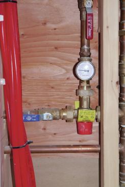 The red knob is part of the Watts mixing valve and can be rotated to adjust the mix of hot and cold water to achieve 120°F. Above the mixing valve is the hot-water supply line to the manifold, complete with a dial thermometer to measure the mixed water temperature and a ball valve to isolate the hot-water manifold.