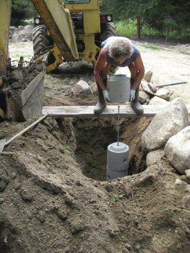 A plank laid across the footing hole provides a bit more control for placing the remaining 60-pound sections and prevents the sides of the hole from caving in.