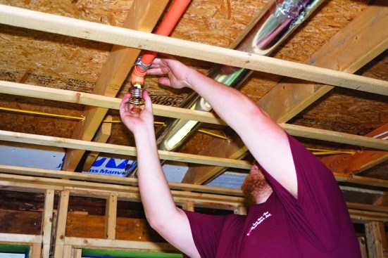 Sprinkler heads are available in ceiling-mounted as well as wall-mounted versions, able to cover an area of about 15 by 15 feet. Here, the installer screws a ceiling head into its fitting.