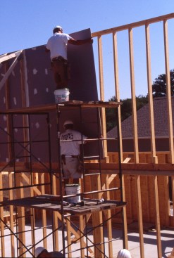 The author’s crew frames a duplex building with units arranged back-to-back. Working from a rolling scaffold on the floor slab, the crew first attaches 5/8-inch Type X gypsum board to the unit separation stud wall.