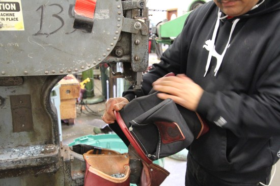 The operator positions the bag for riveting by feeding a pin on the machine through a pre-punched hole in the material. Rivets are used to reinforce areas subject to high stress.