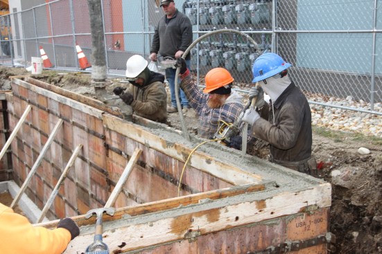 The crew works its way around the wall with pump, vibrator, and shovel.