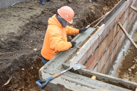 A concrete mason trowels the wall top to a snapped line on the inside of the forms.