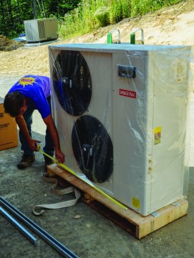 Workers for ReVision Energy install a SpacePak air-to-water heat pump at a custom home in southern Maine. ReVision’s Chris Blaisdell checks the unit’s dimensions.