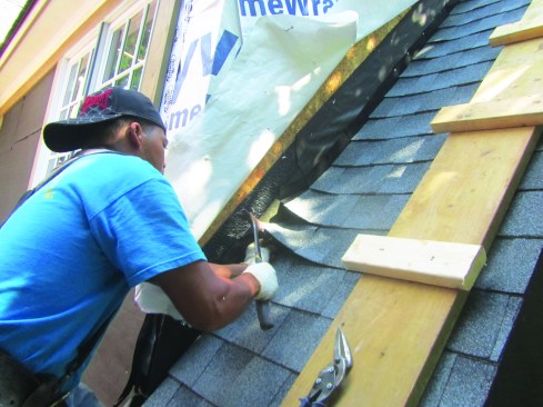 A roofer has cut the housewrap at the joint between the roof and the wall, folding it back so that he can lap it down over the underlayment and step flashing, as the author recommends.