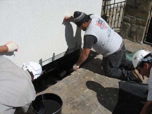 Next, they rolled the hot asphalt onto the wall and the deck edge.