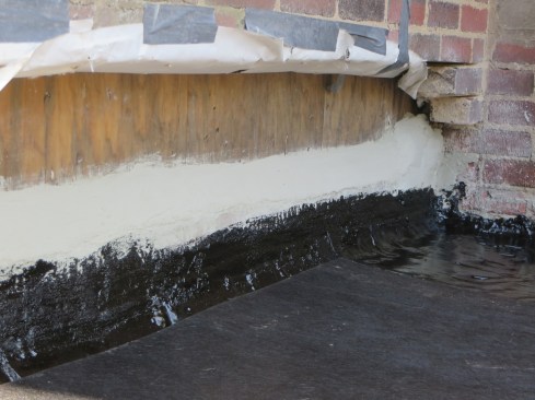 Hot-applied rubberized asphalt is applied to the concrete deck and lapped up onto the primed plywood wall sheathing.