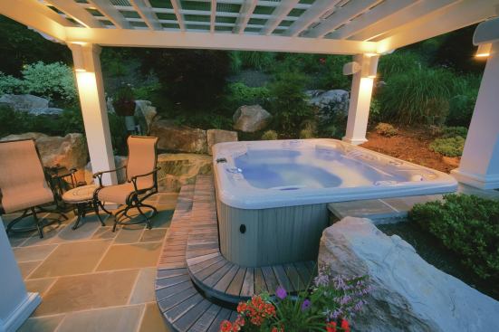 Nestled in a corner with retaining walls and boulders on two sides, this hot tub is protected from sun and rain by a fiberglass pergola topped with double-layered Plexiglas. A sound system and light fixtures add ambiance.
