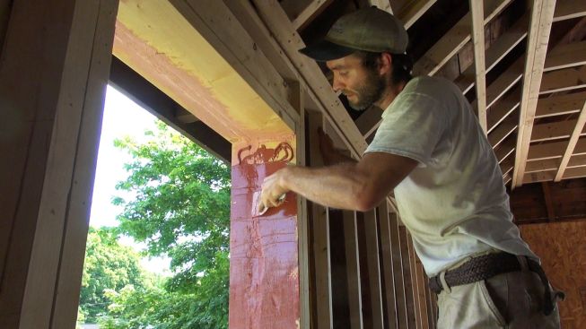 Kelly spreads out the FastFlash to form a continuous coat over the rough, irregular wood framing. Kelly chose the fluid-applied material for this part of the project because he was concerned that it would be difficult to achieve full adhesion on the rough surface using a construction tape.