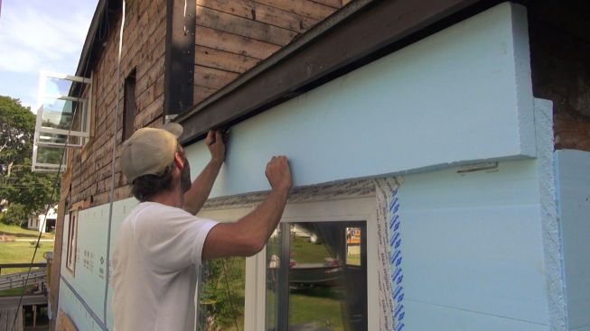 Holding the piece of XPS foam in place, Kelly marks it to lay out cuts for fitting the piece around the existing rafter tails.