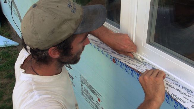 Kelly works a piece of Siga Wigluv tape into the corner at the window bottom and presses the tape firmly against the substrate with a plastic card, supplied with the tape. The tape holds tenaciously to the window frame's vinyl face, even with just a half-inch overlap.