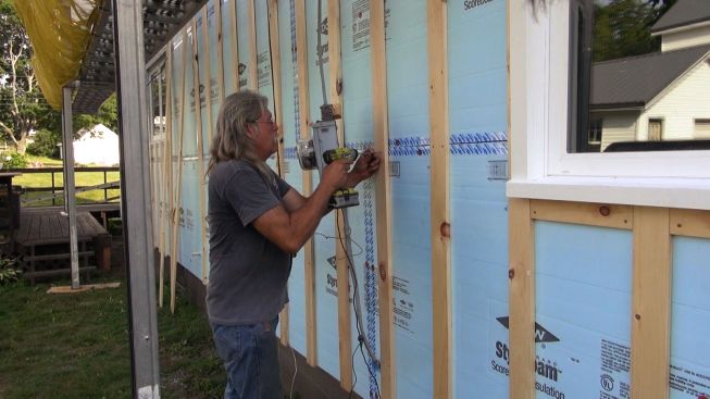 Carpenter Sonny Searles screws a piece of strapping over the foam with GRK screws long enough to sink into the home's sheathing. The crew is using full-width 1x4 strapping for this job, in order to provide good nailing for the vinyl siding to be installed next.