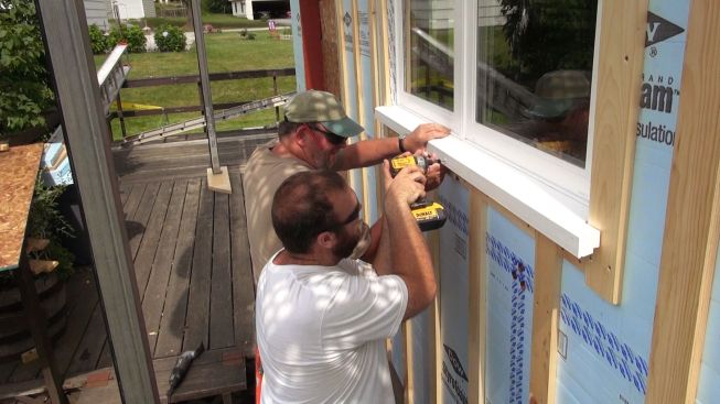 Carpenters Jay Kelleher (rear) and Rick Martin (foreground) screw an Azek finish sill to the rough framing after tape sealing is completed.