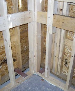 The bottom plates of the inside walls sit directly atop the slab’s perimeter insulation, preventing a direct mechanical connection to the concrete. To hold the walls parallel to the exterior walls, the author used plywood standoffs and sealed beneath the plates with expanding foam.