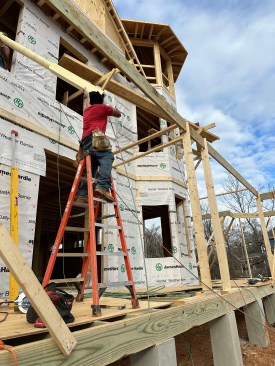 The Queen of Zero framing crew pass a fiberglass ResinArt porch post through the home's second floor window and onto a threaded rod that has been attached to the foundation. 