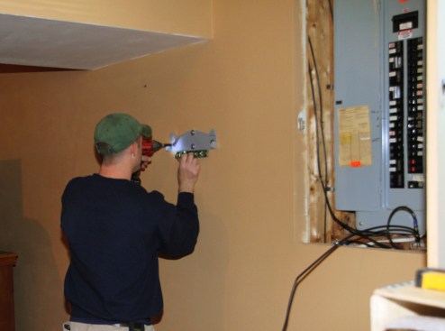 Electrician Scott Millette positions and fastens a mounting bracket for a SolarEdge inverter on the wall of a Vermont home.