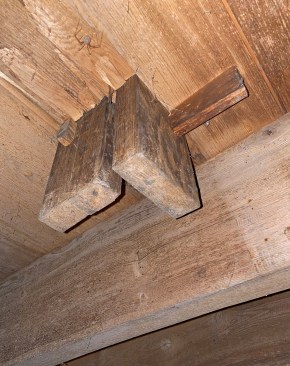Below the base, the end of the newel has two tenons that project through the floor. The tenons are drawn tight to the subfloor by wedges driven into slots in the tenons.