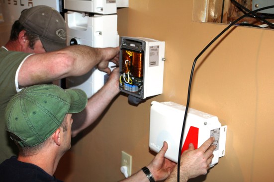 Ritz secures the transformer to the mounting plate while Millette positions the system's smart meter enclosure.