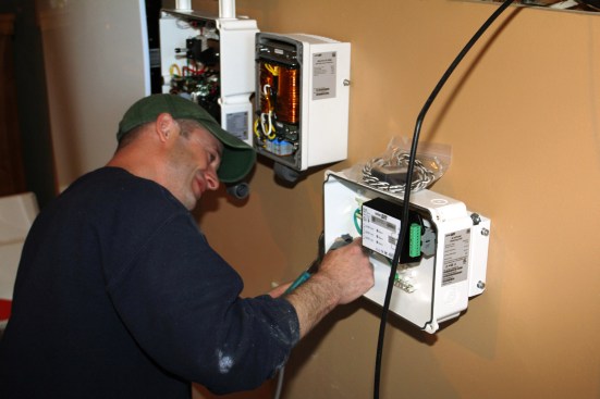 Millette attaches a conduit fitting to the smart meter enclosure. The StorEdge meter works in tandem with the inverter, sensing whether the system is producing or demanding power. Two circuit transformers or CTs (in plastic bag sitting on top of the housing) are installed on either side of the meter to monitor the amperage passing through the system.