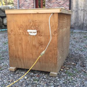 An oversized lid caps the box so that water can't infiltrate the contents. A power strip's cord is fed through a notch near the top and connected to an extension cord. Handles recycled from a window delivery make the unit easier to lift.