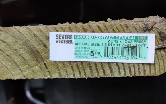 Preservative treatment lumber tag on one end gives the size of the 2x12, along with the AWPA UC4A level that indicates it is suitable for “Ground Contact.”