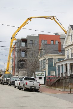 A concrete pump truck's boom reaches high overhead and back to the rear of a tight building site in Portland, Maine. Great Falls Construction (Gorham, Maine) is overseeing construction on the four-family infill project in a rapidly developing neighborhood in Portland's East End peninsula.