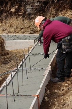 A concrete mason with JB Concrete Foundations hooks bent half-inch rebar under the horizontal rebar in a freshly poured footing on a multifamily infill site in Portland, Maine.