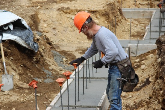 A concrete mason with JB Concrete Foundations (Bridgton, Maine) places safety caps on projecting rebar during a footing pour for Great Falls Construction in Portland, Maine.