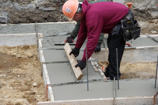 A concrete mason marks the position for vertical rebar using a jig made with screws set into a 2x4.