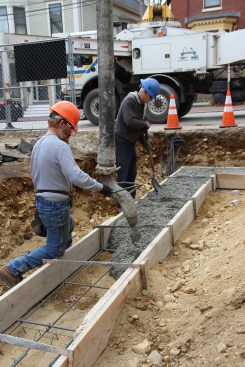 Steel brackets hold and brace the 2x8 sawn lumber footing forms at the correct width as masons us a pump on the street to place the concrete.