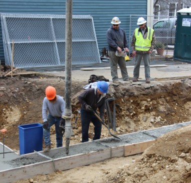A concrete pump boom truck operator controls the flow of concrete using a remote control as masons complete the footing pour for an infill project in Portland, Maine. Constrution supervisor Jeff Barker, of Great Falls Construction, looks on.