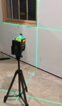 The laser is mounted on a camera tripod leveling a window.