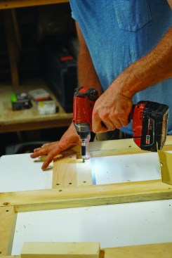 He screws down the wood to the melamine surface of his worktable.