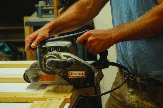Where necessary, he sands the wood with a belt sander to even up any inconsistencies in the thickness of the lumber.