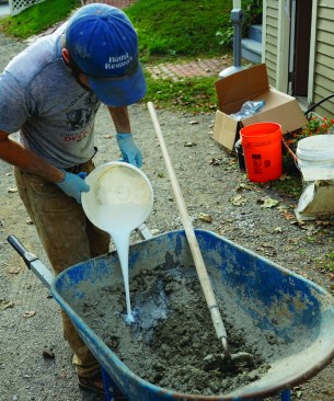 Then he places them in the wheelbarrow in small batch amounts, and adds pre-mixed water and acrylic fortifier until the material is well wetted.