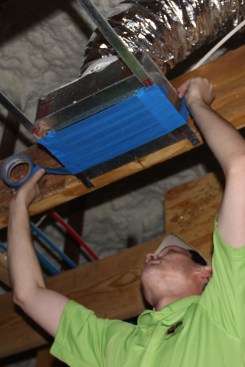 Technician Adam Hovis temporarily masks an energy recovery ventilator (ERV) outlet in preparation for a blower-door test.