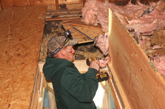 Before rebuilding an attic hatch, home-performanceretrofit technician Marcus Clement builds a plywood dam around the attic floor opening to contain blown cellulose insulation.