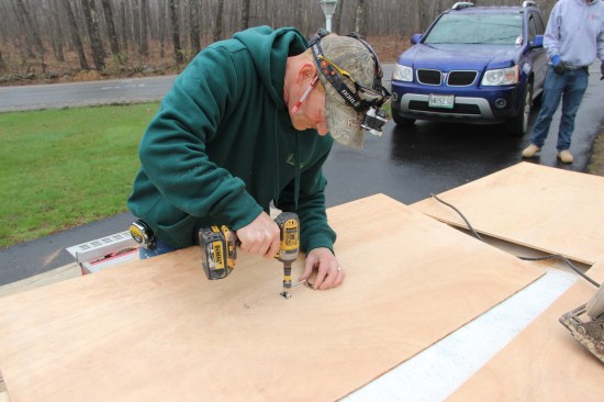 After measuring the opening and cutting a piece of plywood to size, he screws a cabinet door handle to the center of the door.