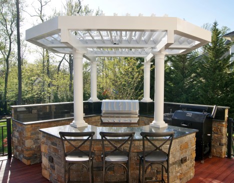 This outdoor kitchen features granite countertops and cabinets faced with stacked stone. Rain or shine, shelter is provided by an Equinox louvered octagonal pergola, supported by custom PVC columns.