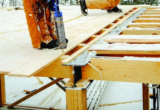 Working in a light snowstorm, the crew glued and nailed tongue-and-groove pine boards to the sawn beam framing.