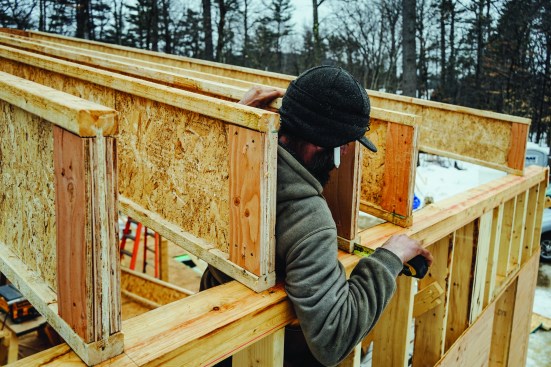 The roof assembly includes load-bearing LVL rim joists that span over windows in the end walls. Matt Friel measured from the edge of the beveled bottom plate to allow room for the LVL.