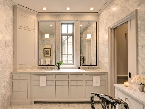 As part of the second phase of a whole-house remodel, DeRhodes Construction redesigned this master bathroom, incorporating custom features and details. On the marble wall of the vanity, two piece mirrors border a narrow window. The team mitered, beveled, and fabricated marble to give the impression of large columns and beams. Below, custom, hand-painted cabinetry provides storage.