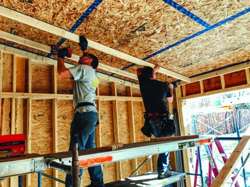OSB applied to the underside of the truss roof and taped with ProClima tape formed the air barrier for the building's roof assembly. Here, Dwyer and a carpenter screw 2x4 strapping on edge underneath the ceiling OSB to create a chase for wiring and ERV tubing, within the conditioned envelope. This approach kept ceiling penetrations to a minimum.
