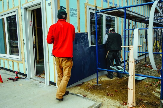 Above, David Kelly and carpenter Jay Kelleher set a Hardie fibercement panel onto the strapped wall of the house. The cladding system is labor-efficient in theory, but does involve a learning curve, said Kelly and Dwyer.