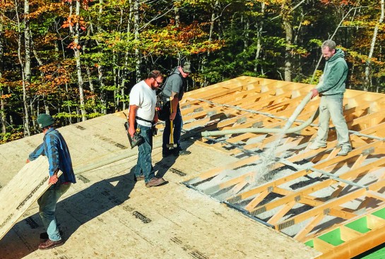 As Matt Damon of Penobscot Home Performance places loose-fill cellulose insulation from above, carpenters follow along behind to install roof sheathing. Insulating and sheathing the entire roof and applying weather-tight roof underlayment took one working day, said Dwyer.