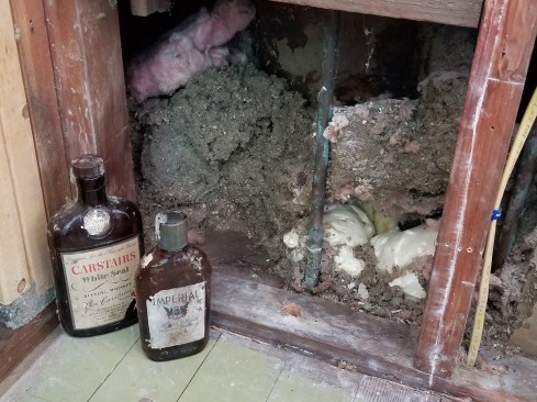 Removing blown-in insulation from around the tub in the adjacent bathroom, exposed two empty bottles stashed there by some former tradesman. One can only speculate as to the actual source of this unsavory time capsule.