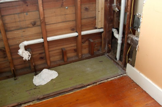 The new exit plumbing for the kitchen sink and dishwasher enters the chase behind the tub with a sweep 90, and then reverses slightly so that the plumbing avoids the floor framing below. The pipe from the top of the T-Wye is for the required plumbing vent.